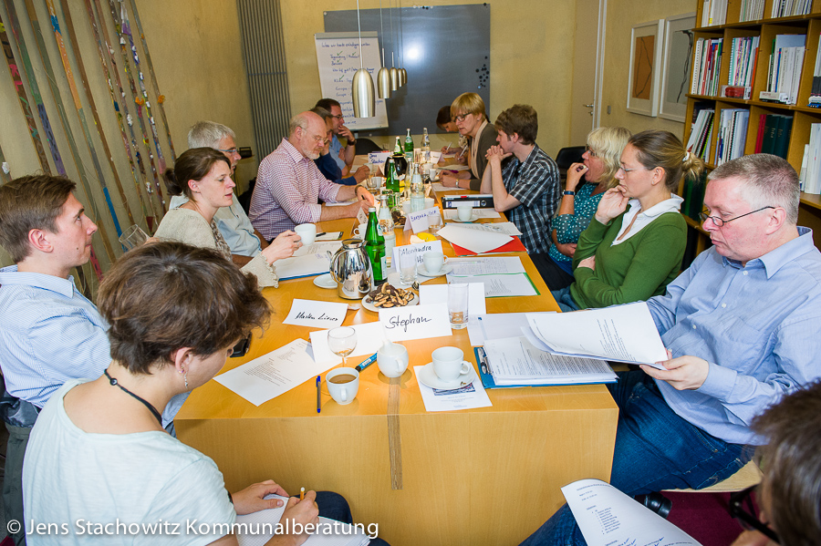 Persoen sitzen um einen Tisch und essen, trinken, reden.