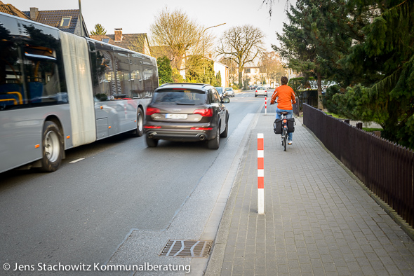 Bus und SUV begenen sich auf der Fahrbahn, Radfahrerin nutzt den Gehweg.