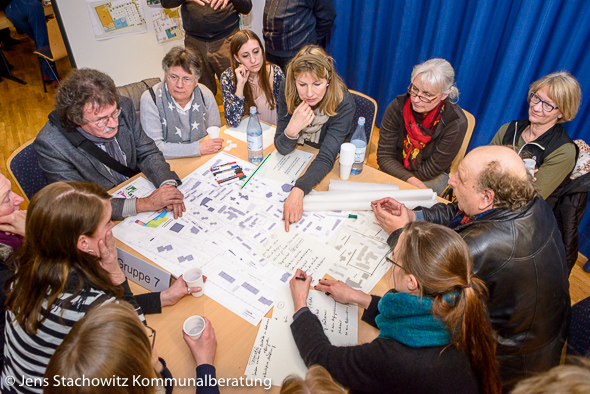 Personengruppe sitzt um einen Tisch herum und diskutiert einen Plan