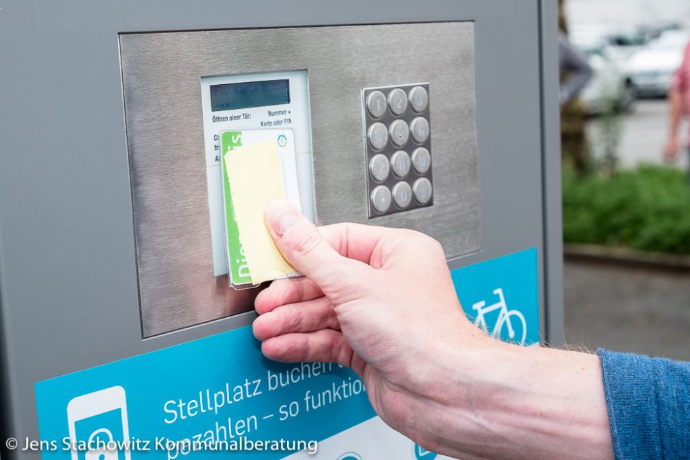 Hand führt Cipcarte zur Bedieneinheit des Fahrradcontainers.