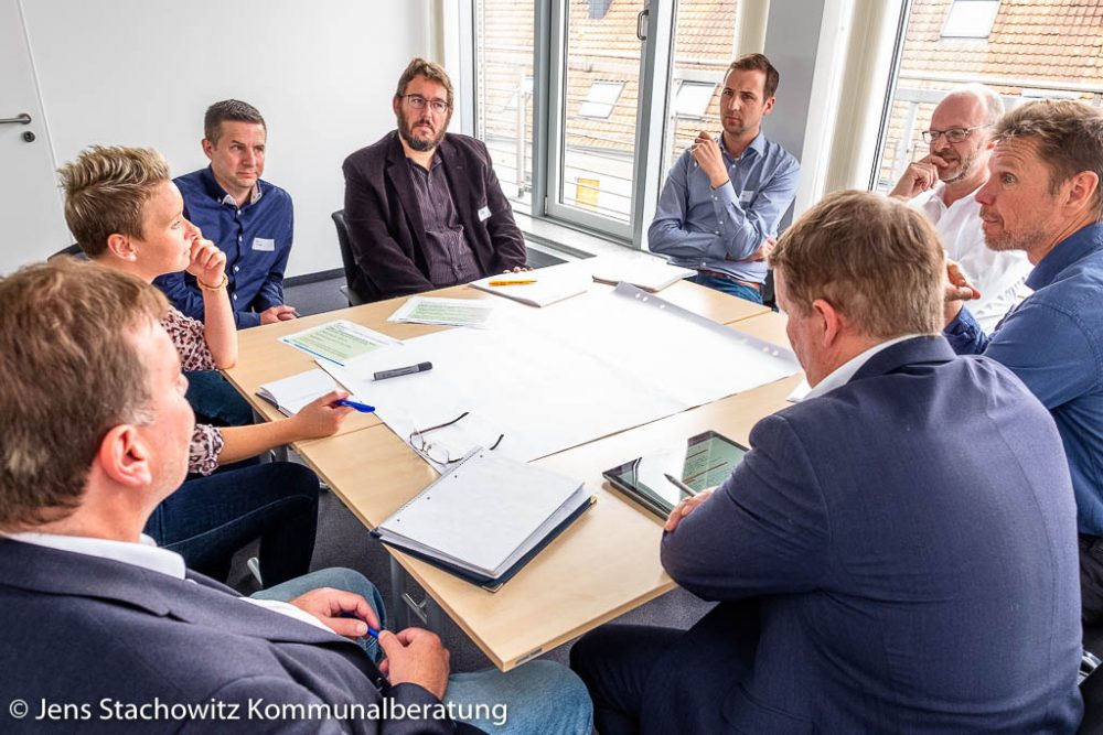 8 Personen sitzen um einen Tisch und beraten.