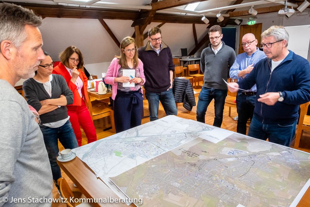 8 Personen stehen um einen Stadtplan und hören einem Arbeitsgruppensprecher zu.